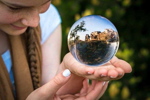 Foto do rosto de uma mulher de perfil com as mãos estendidas e sobre elas está uma bola de cristal. A foto ilustra o artigo "Como analisar e escolher um oraculista para fazer suas leituras?" do site Ori Mystyco.