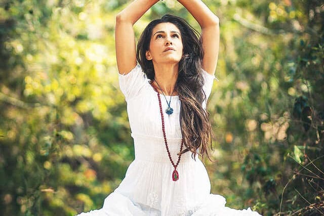 Foto de mulher com vestido branco meditando no jardim. A foto ilustra o artigo "Yoga: conexão com a mente, corpo e espírito" do site Ori Mystyco.