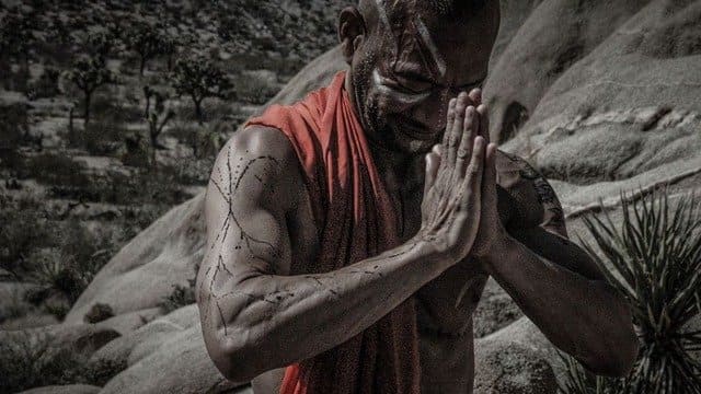 Foto de um africano sentado em uma floresta com as mãos impostadas em forma de oração. A foto ilustra o artigo Seus ancestrais não estão mortos do site ori Mystyco.