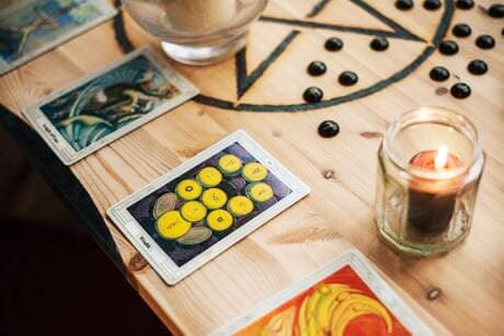 Foto de 3 cartas do Tarot rider Wait em cima de uma mesa. As cartas estão em pé, apoiadas em uma pano roxo. Atrás das cartas há também uma vela de 7 dias acessa. A foto serve para ilustrar o artigo Tarot Online Grátis - 3 cartas (Passado, Presente e Futuro) do site Ori Mystyco.